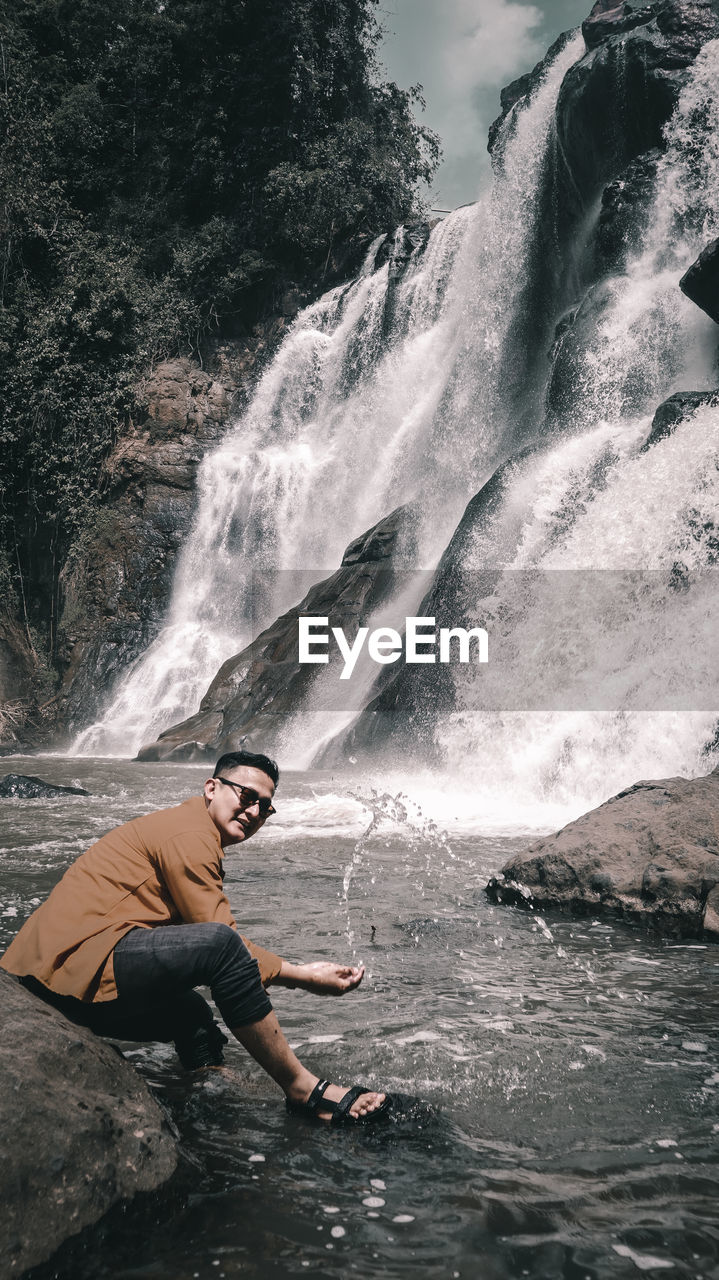 Full length of man splashing water by waterfall