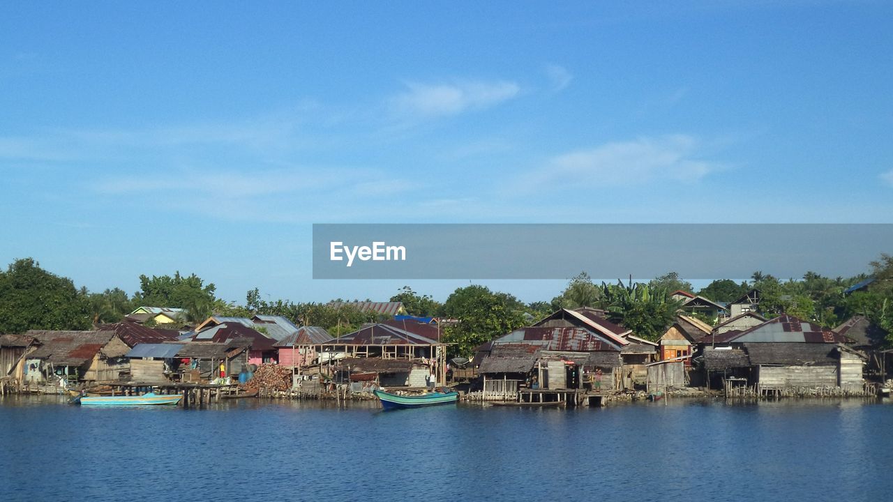 Houses by lake and buildings against sky