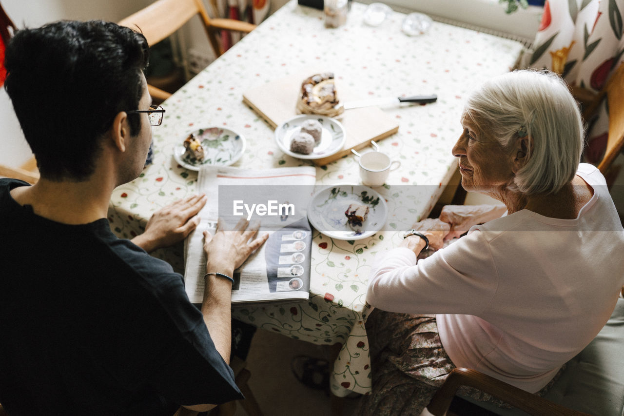 High angle view of male nurse and senior woman reading newspaper at dining table