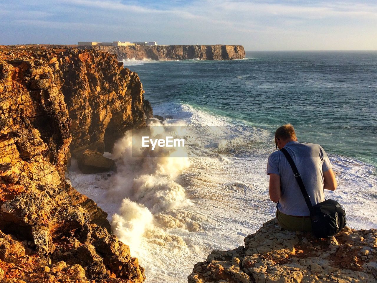 Rear view of man sitting on cliff by sea