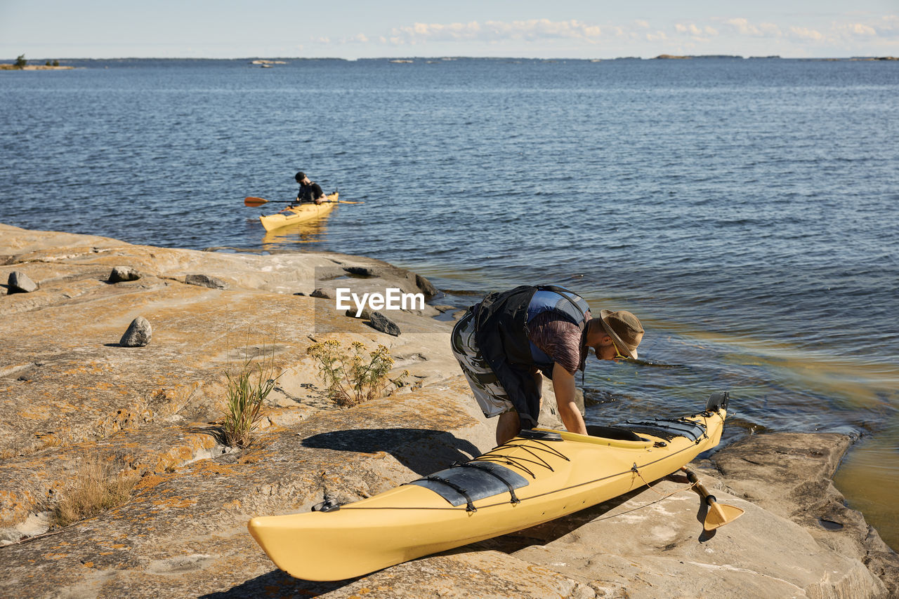 Man on rocky coast preparing kayak for a trip