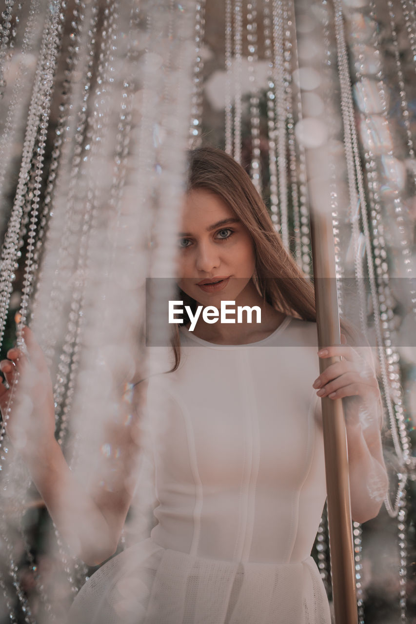 Portrait of beautiful young woman standing against curtain