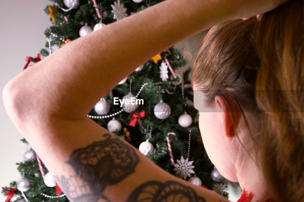 Close-up of woman tying hair while standing by christmas tree at home