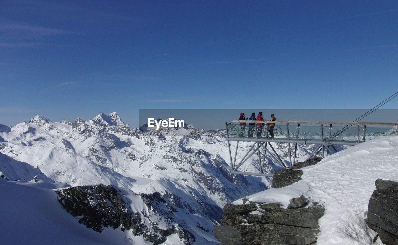 PEOPLE ON SNOW COVERED MOUNTAIN AGAINST BLUE SKY