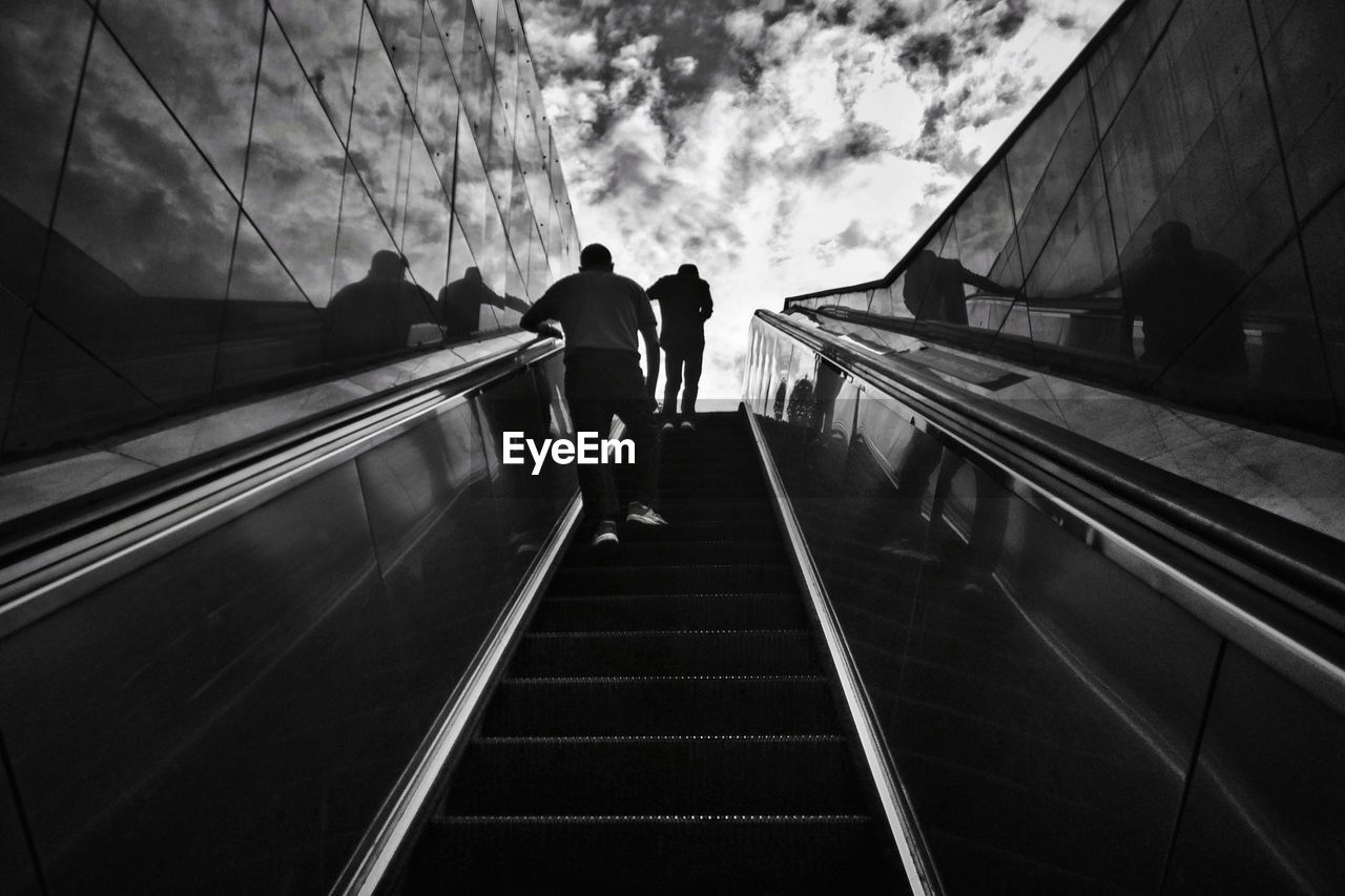 REAR VIEW OF PEOPLE ON ESCALATOR AGAINST SKY