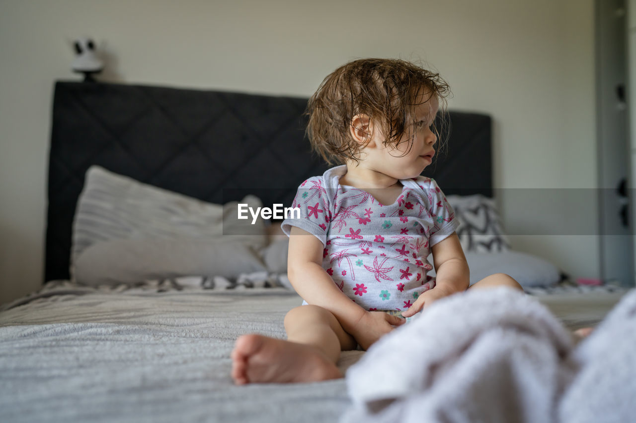 portrait of cute baby girl sitting on bed at home