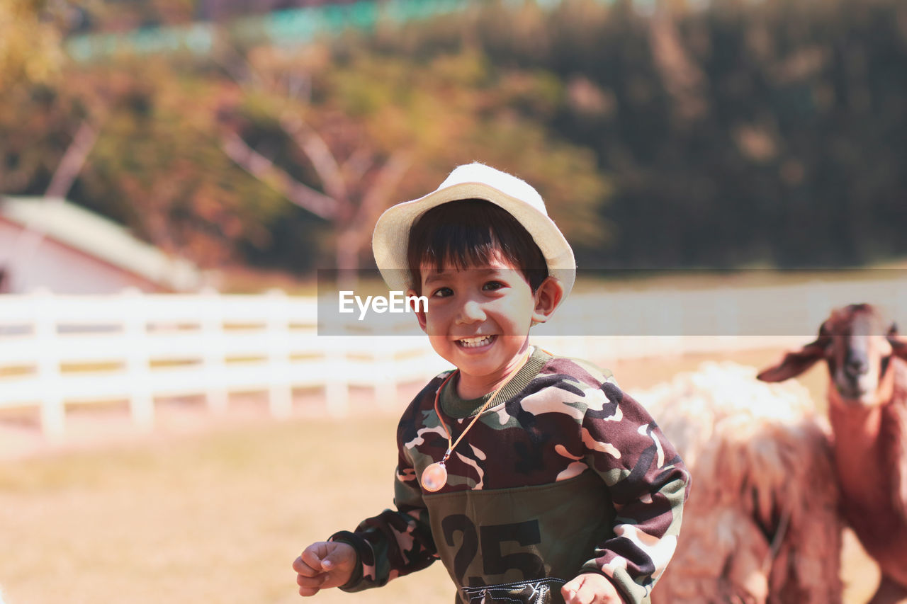 Portrait of smiling boy wearing hat standing outdoors at farm