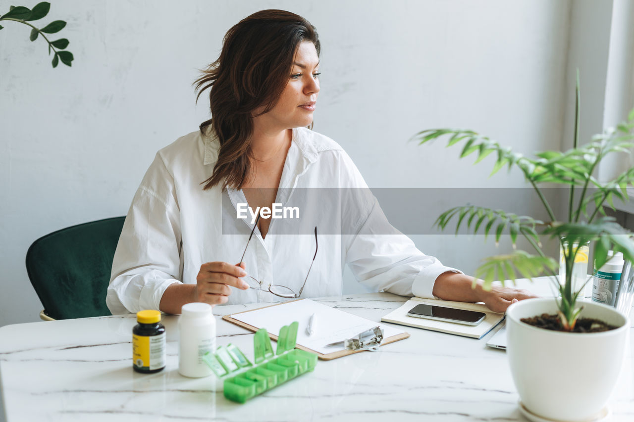 Young brunette woman nutritionist plus size in white shirt working at laptop in bright modern office