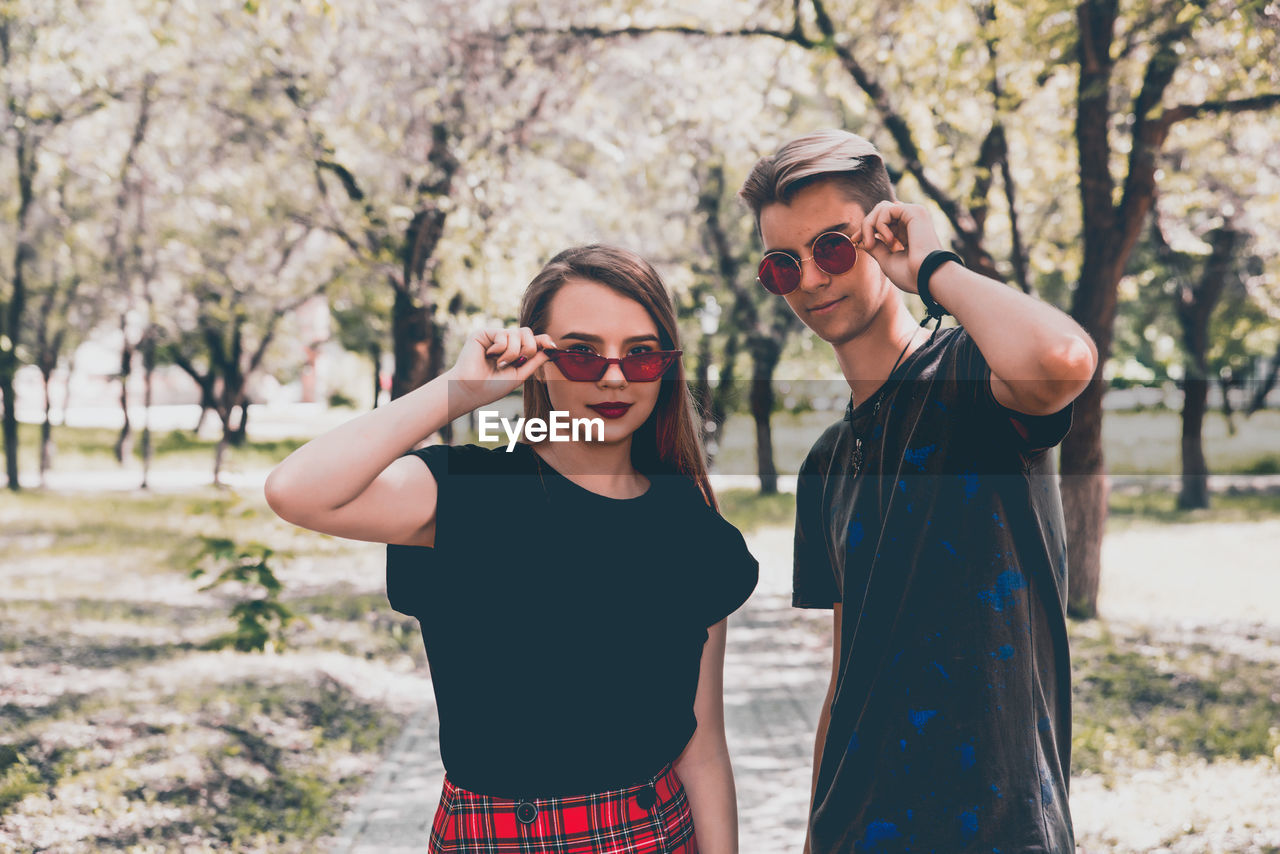 Couple wearing sunglasses standing against trees
