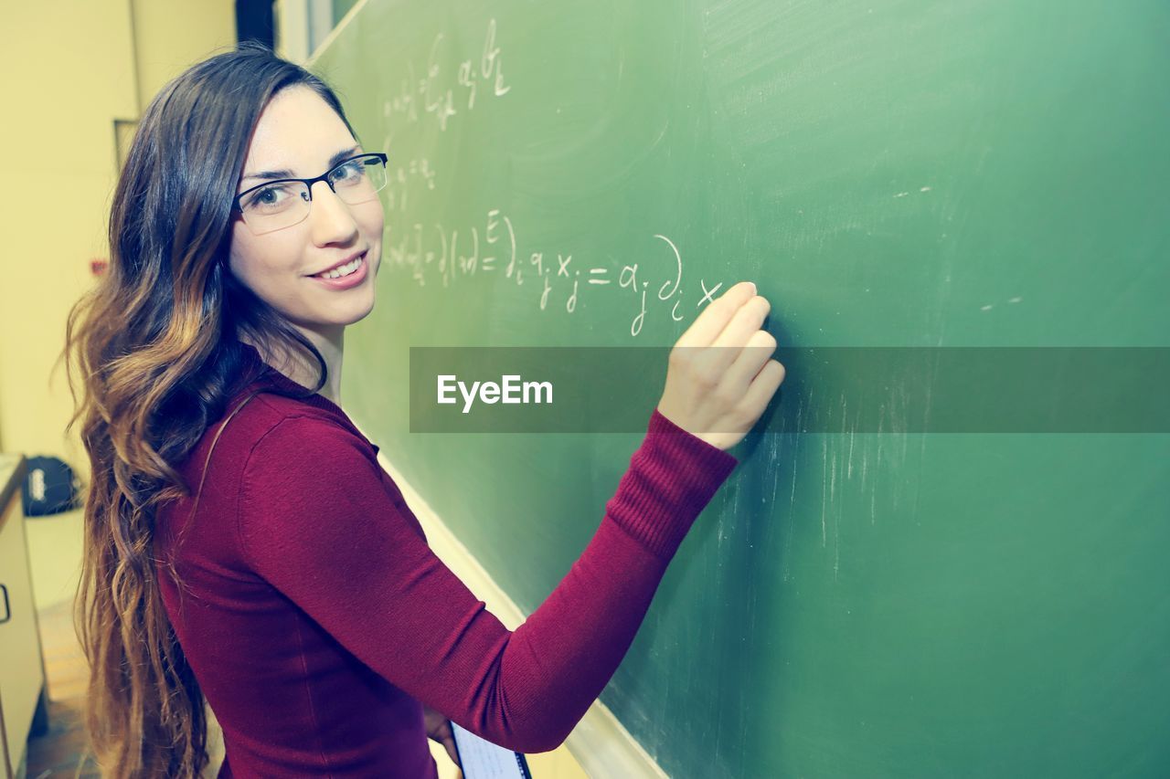 blackboard, board, education, school, classroom, learning, women, student, school building, teacher, glasses, one person, indoors, building, adult, smiling, young adult, architecture, university, eyeglasses, long hair, teaching, portrait, intelligence, green, happiness, standing, hairstyle, waist up, female, emotion, child, studying, science, copy space, teenager, university student, clothing, casual clothing, person