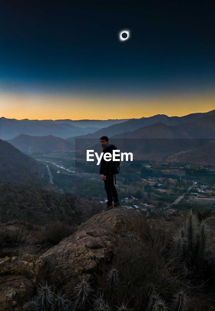 Man standing on mountain peak against eclipse