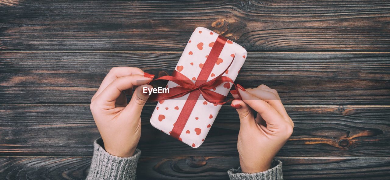 Cropped hands of woman opening gift on table