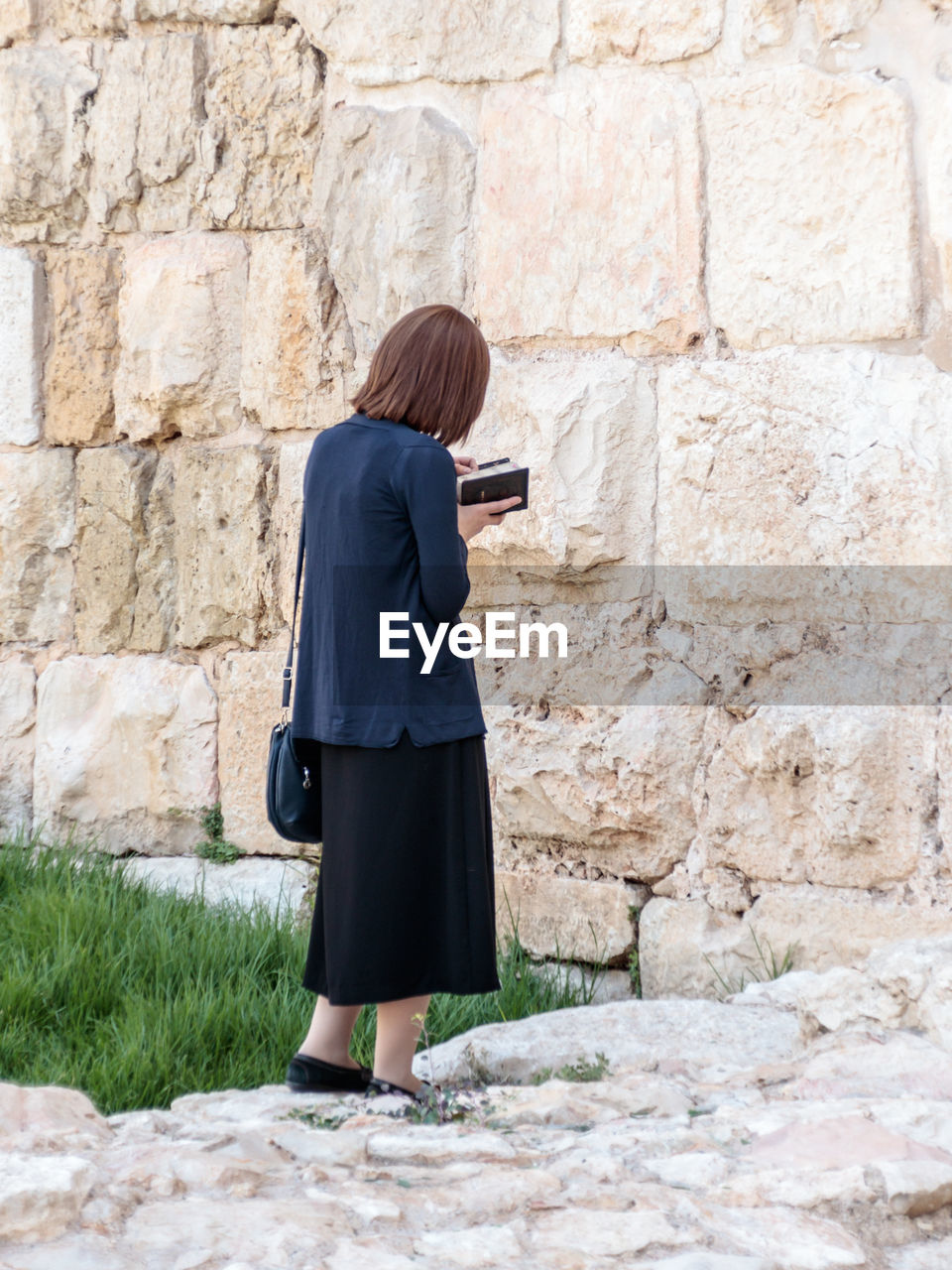 Rear view of woman standing against stone wall