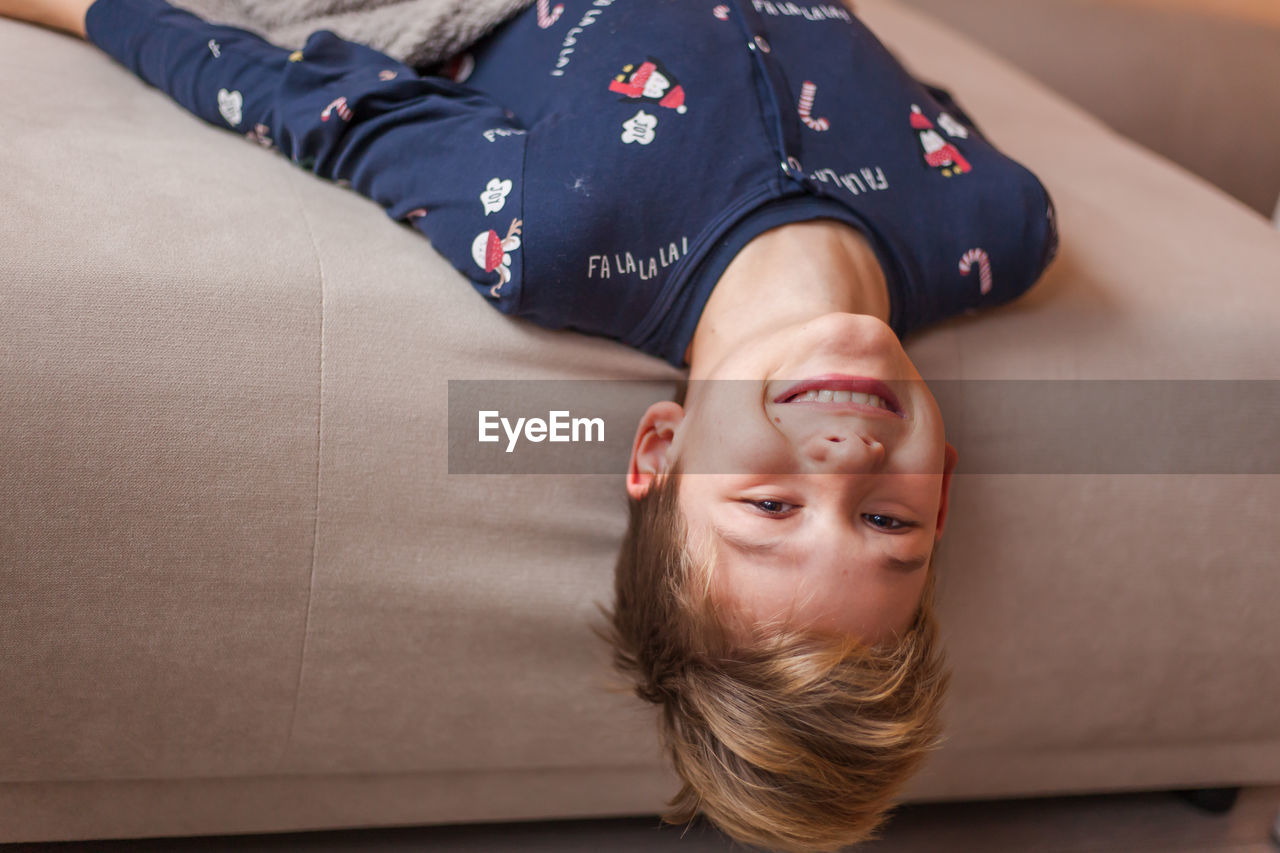 Portrait of happy boy lying upside down on sofa