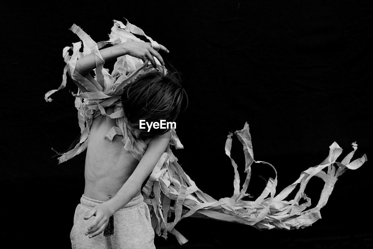 Shirtless boy dancing against black background