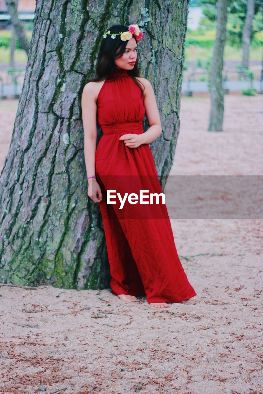 Woman in red dress standing against tree trunk