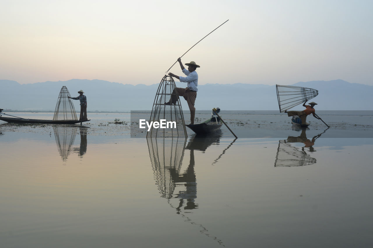 Fishermen fishing in lake against sky during sunset