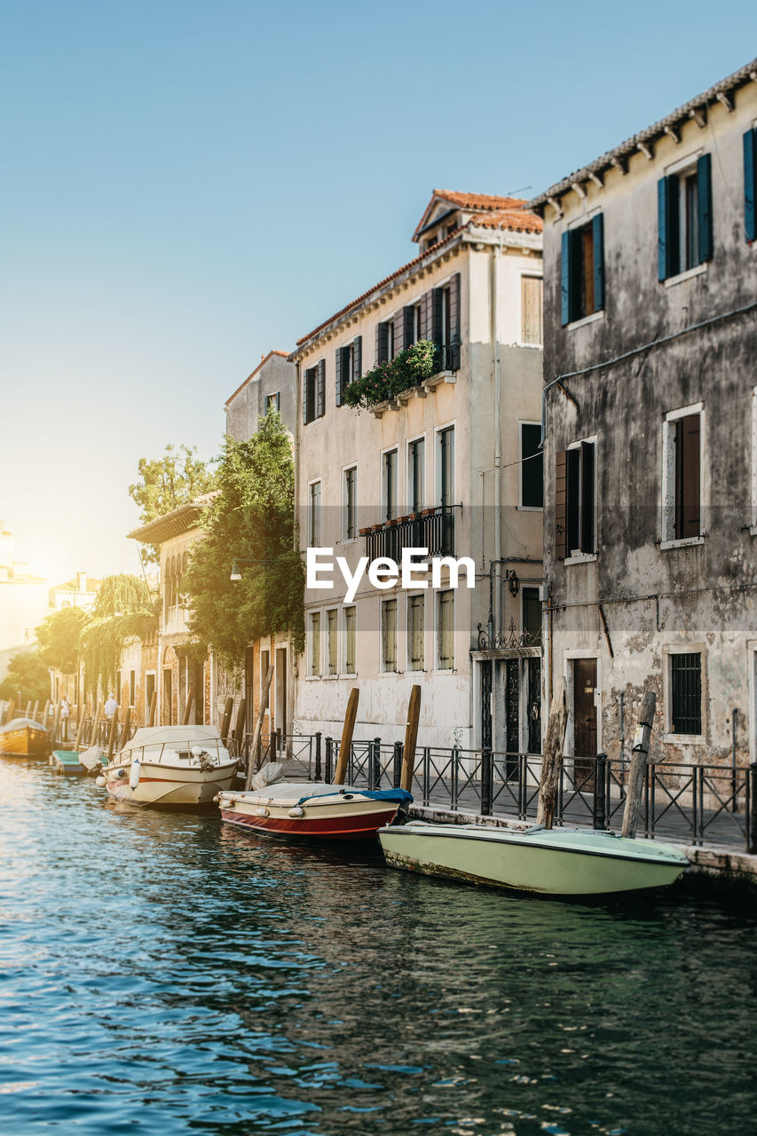 Boats moored on canal by buildings against clear sky