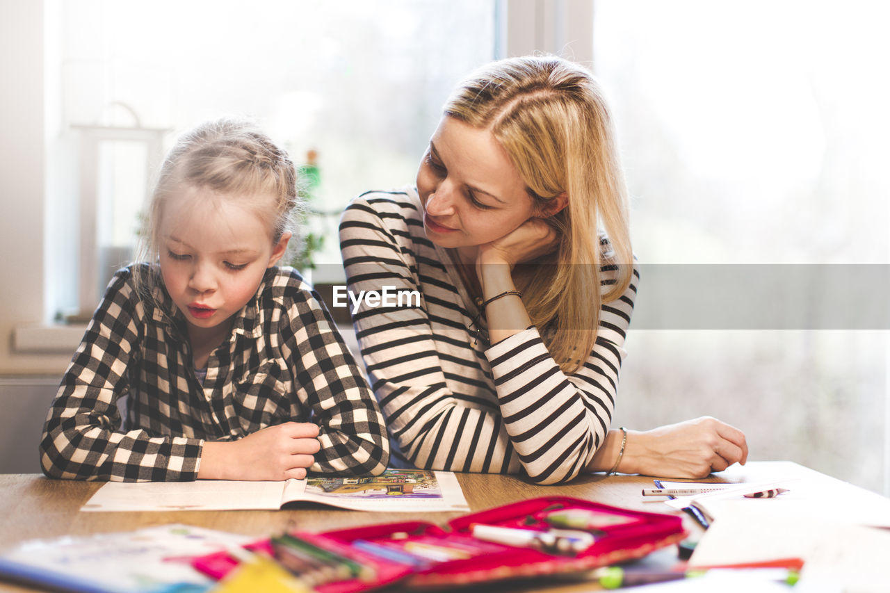 Girl studying while sitting with mother at home