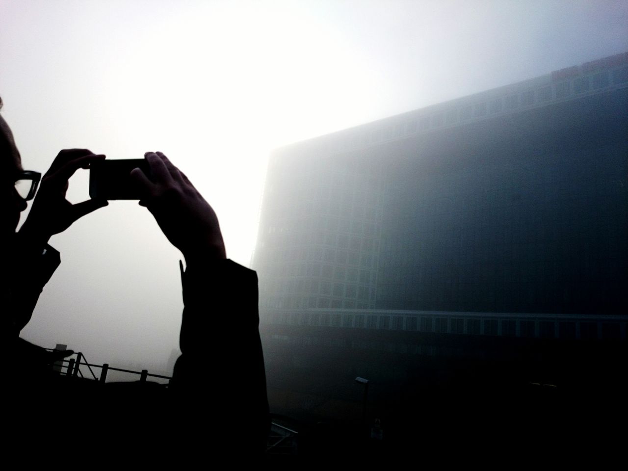 Cropped image of man photographing building in foggy weather