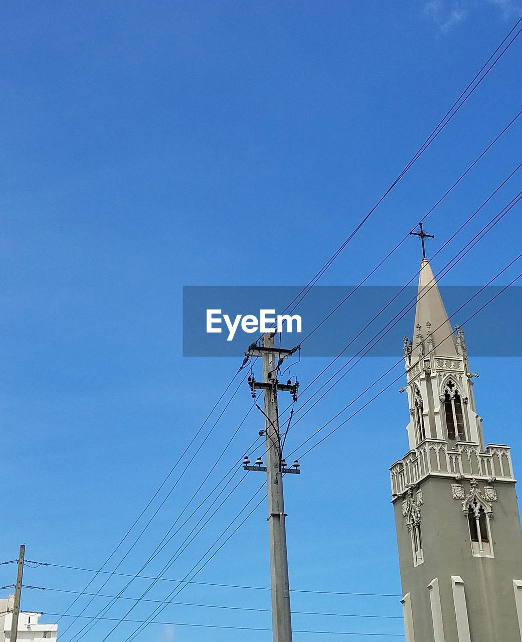 Low angle view of telephone line by church against clear blue sky