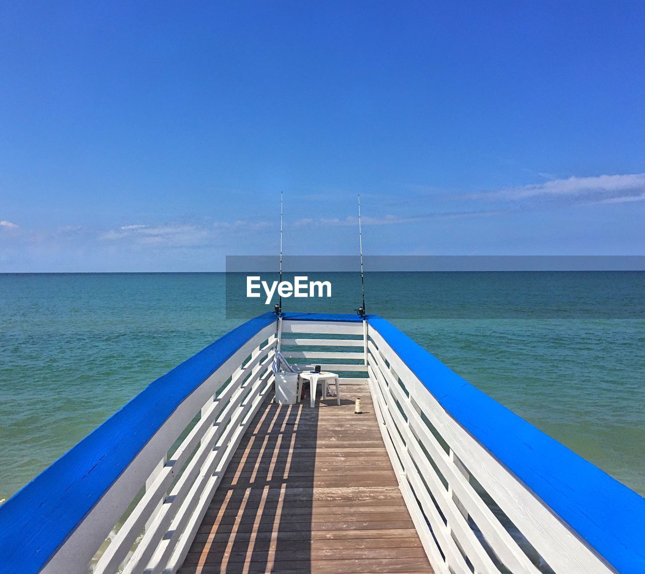 Fishing rods on pier by sea against sky