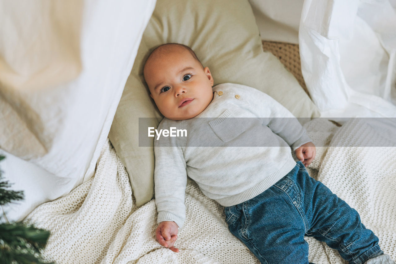 Cute smiling baby boy in beige 5-6 month looking at camera on bed with knitted blanket