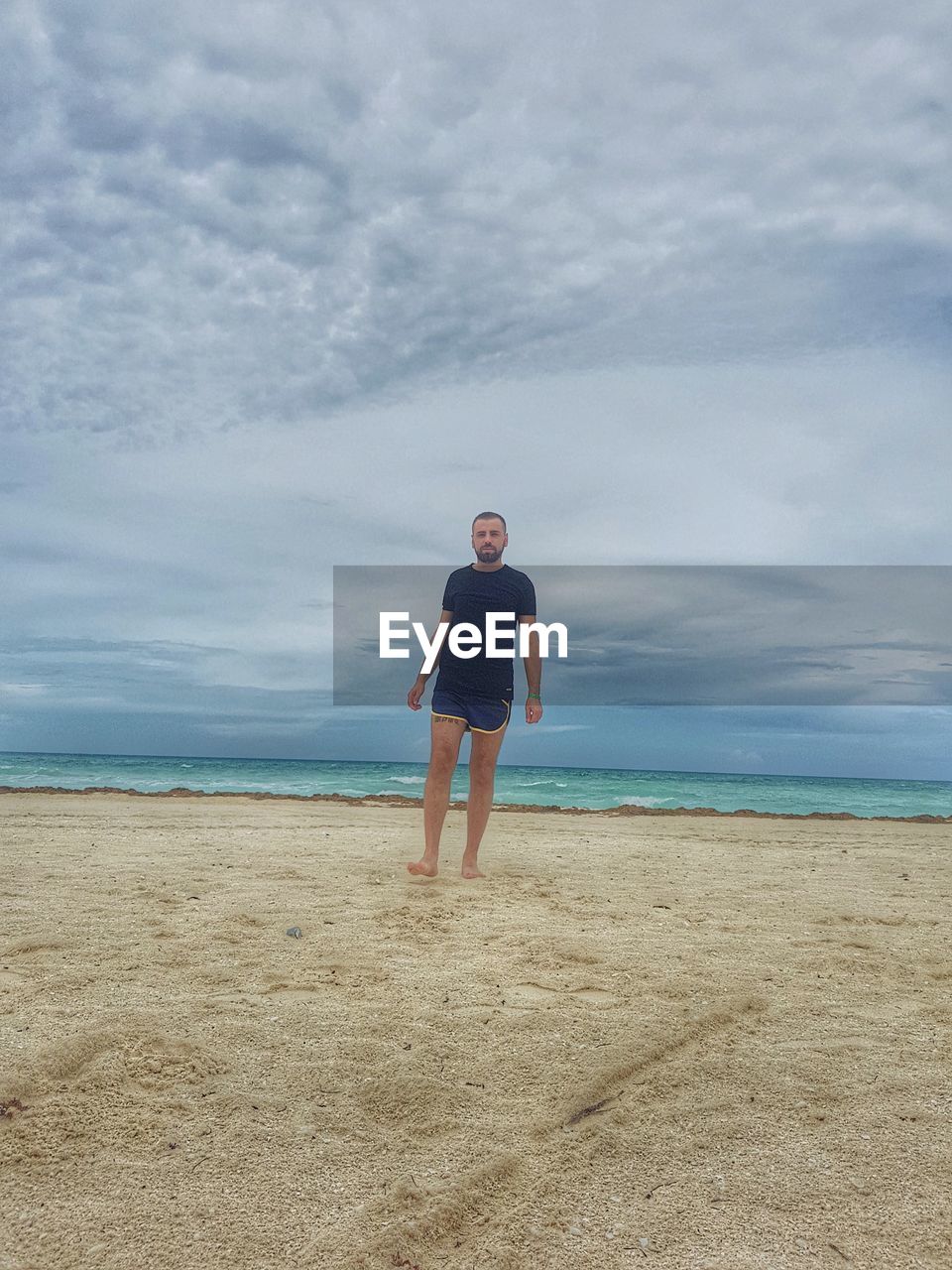 BOY STANDING ON BEACH AGAINST SKY