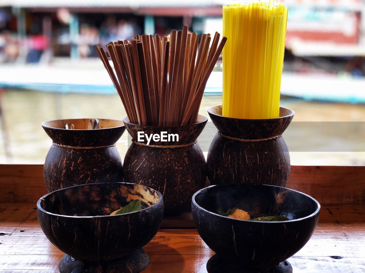Close-up of wooden bowl with chopsticks and drinking straws on table
