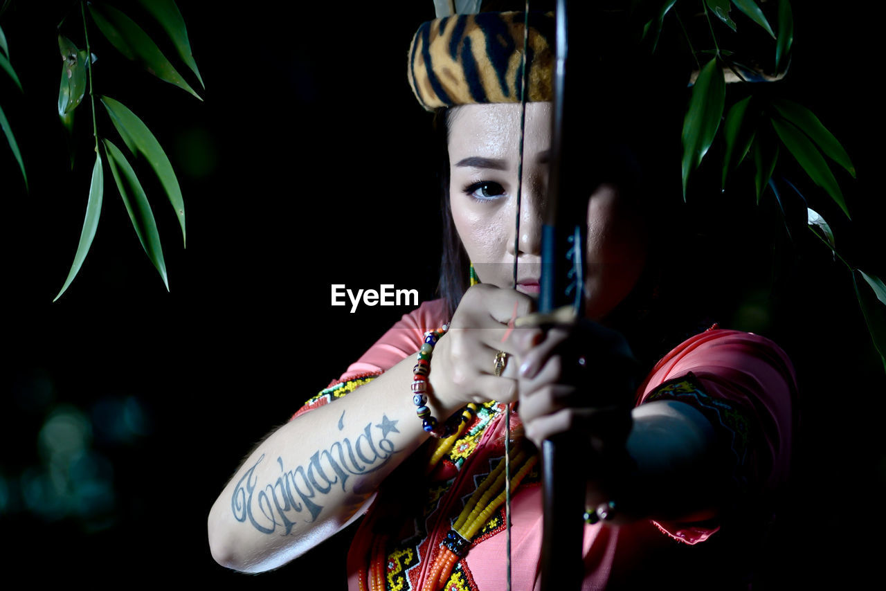 Portrait of young woman holding longbow outdoors