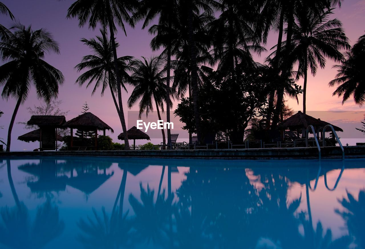 Silhouette palm trees and hut reflecting in swimming pool during sunset sky