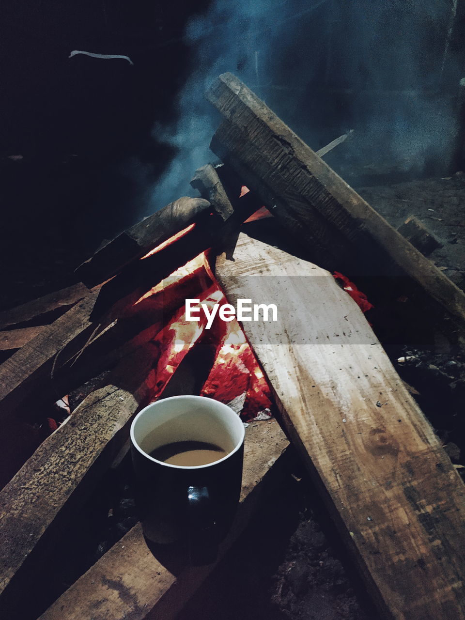 Coffee cup on firewood by campfire at night