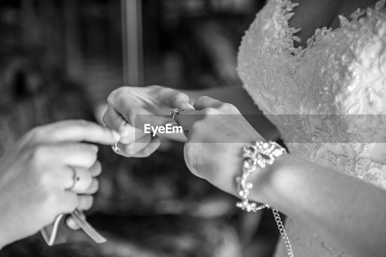 Close-up of bride putting rings in finger with person