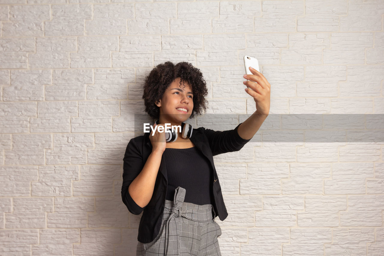 YOUNG WOMAN PHOTOGRAPHING WHILE STANDING AGAINST WALL