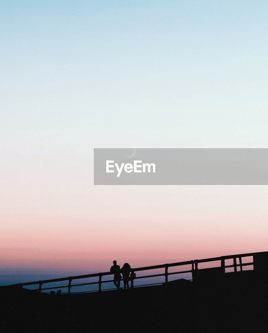 sky, horizon, dawn, silhouette, nature, sunrise, sea, railing, water, beauty in nature, morning, scenics - nature, copy space, tranquility, ocean, tranquil scene, clear sky, coast, men, horizon over water, beach, moon, land, architecture, outdoors, leisure activity, group of people, bridge, lifestyles, idyllic, built structure, transportation, sun, walking, travel destinations, travel, women