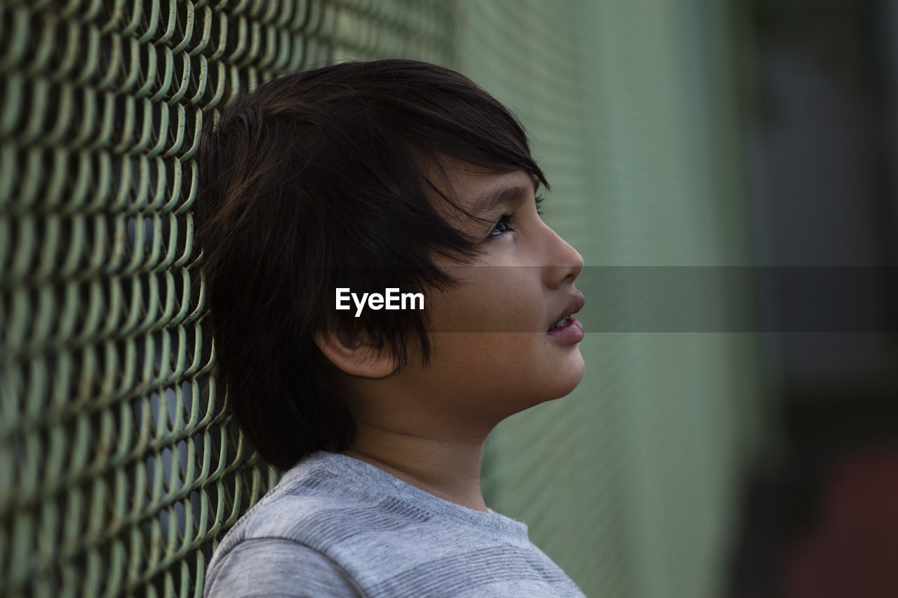 Close-up of cute boy leaning on chainlink fence