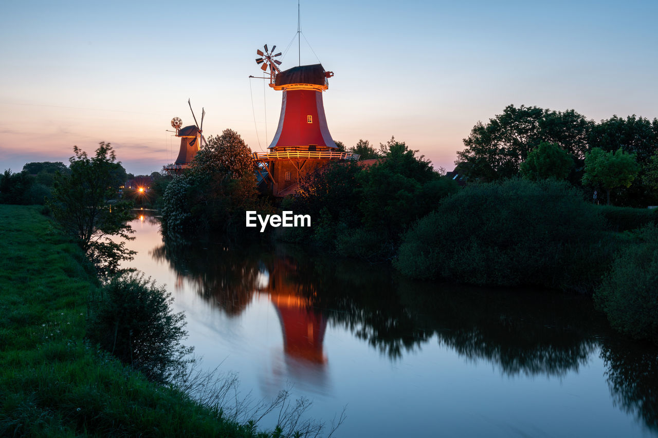 Scenic view of canal by traditional windmills against sky during sunset