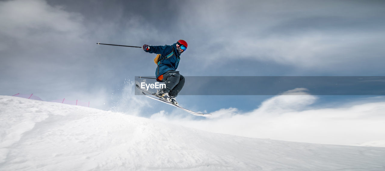 A sportsman skier in ski equipment jumps down a steep snowy slope of a mountain against the backdrop