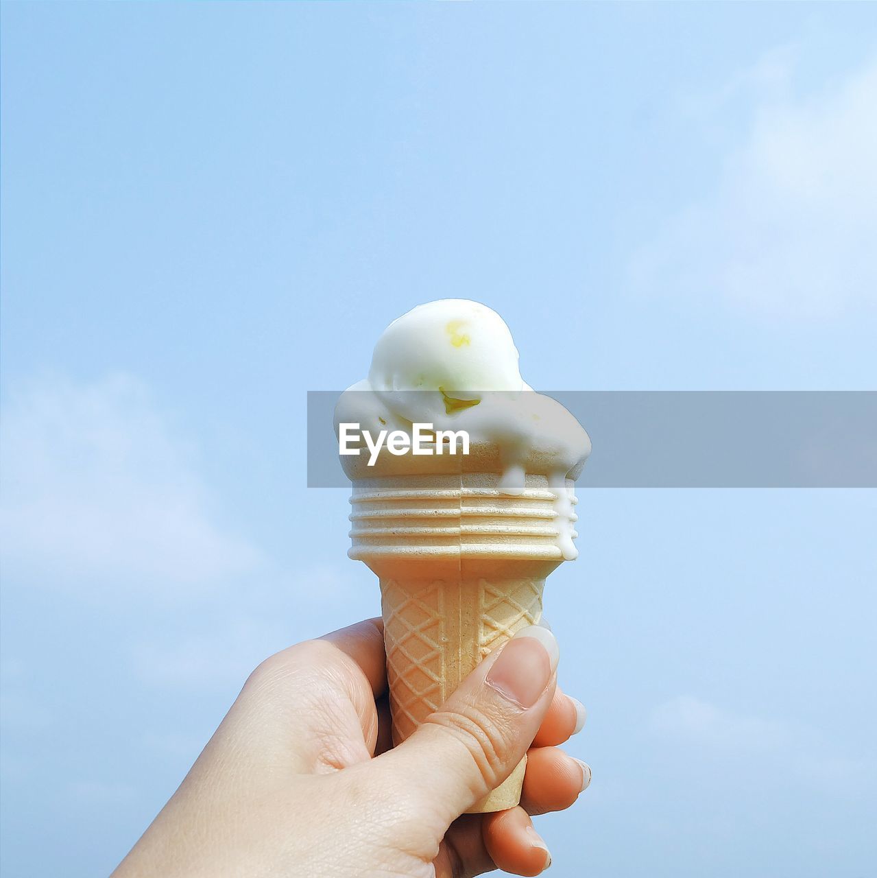 Cropped woman holding ice cream cone against sky