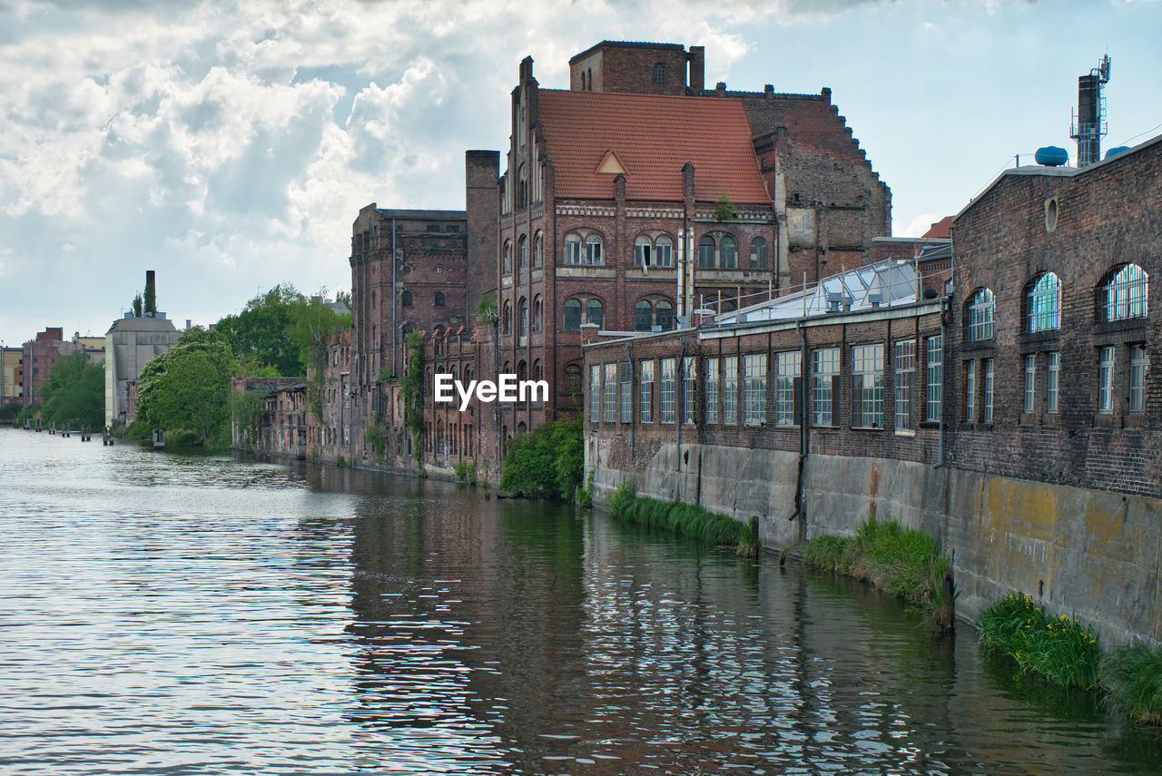 Buildings by river against sky