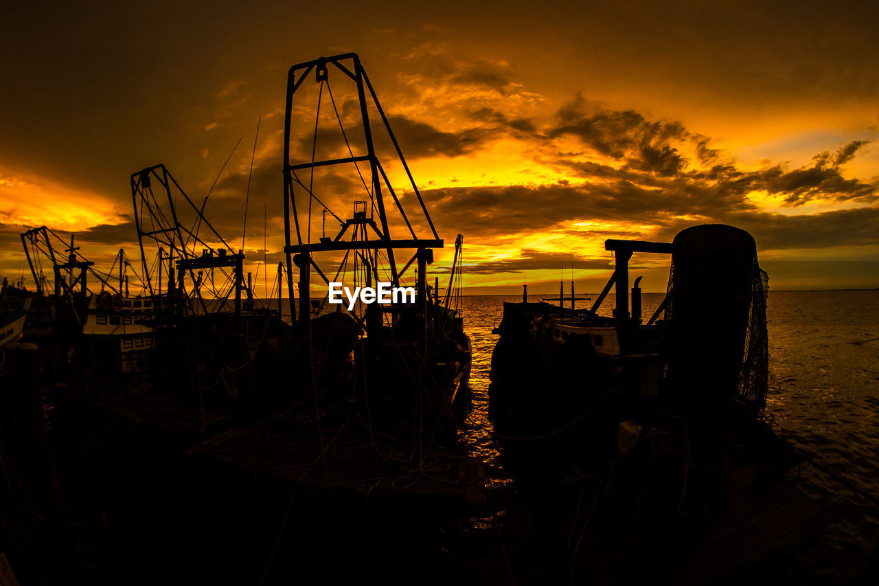 SILHOUETTE FISHING BOATS ON BEACH AGAINST ORANGE SKY