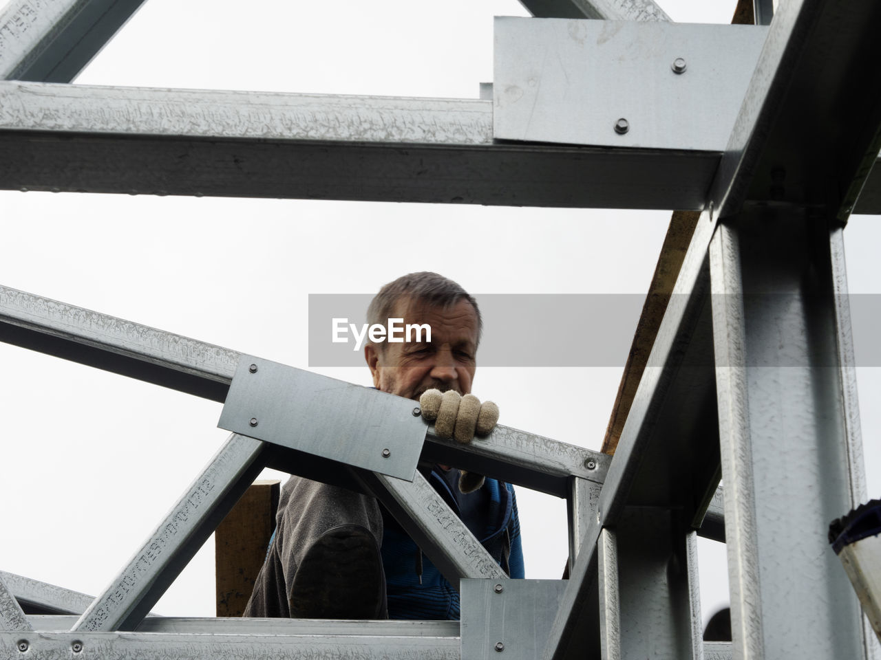 Low angle view of senior man working on metallic structure at construction site against sky