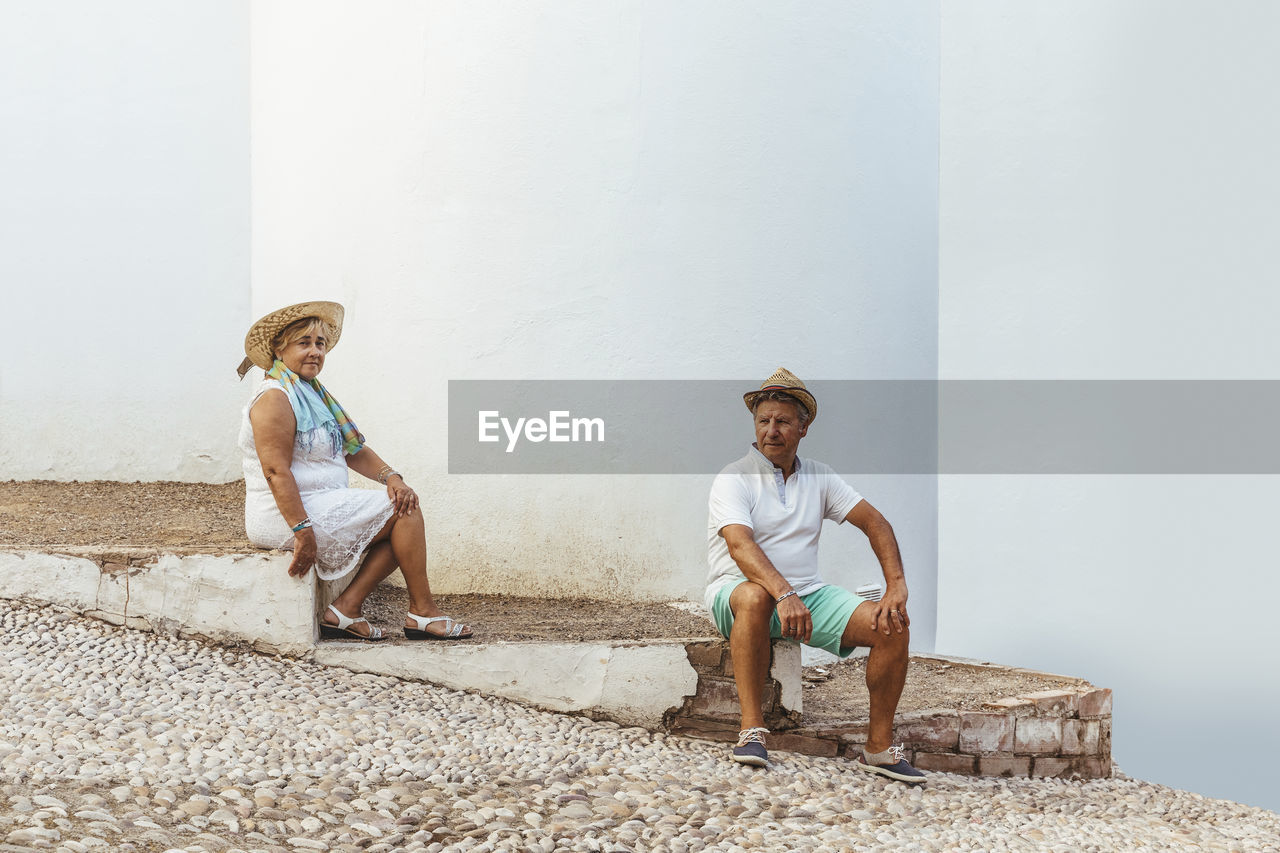 Senior tourist couple sitting on steps in a village, el roc de sant gaieta, spain
