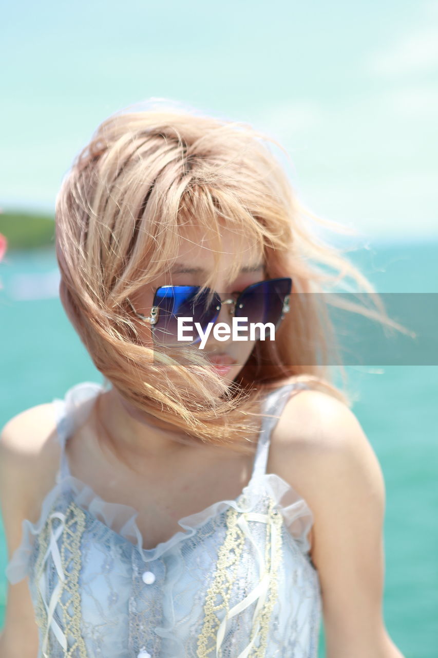 Portrait of young woman wearing sunglasses against sea
