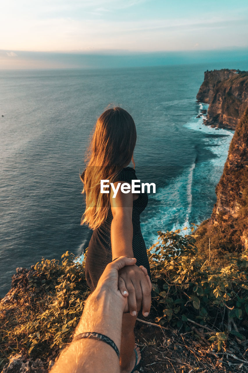 Couple holding hands at beach against sky