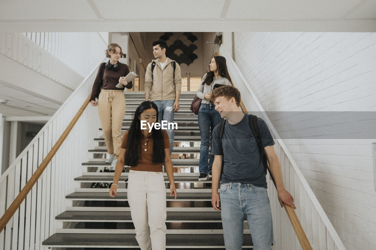 Happy multiracial male and female students moving down on steps in university