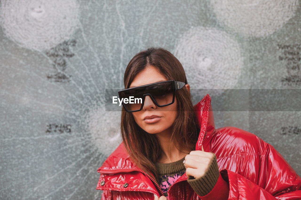 Portrait of smiling young woman wearing sunglasses against wall