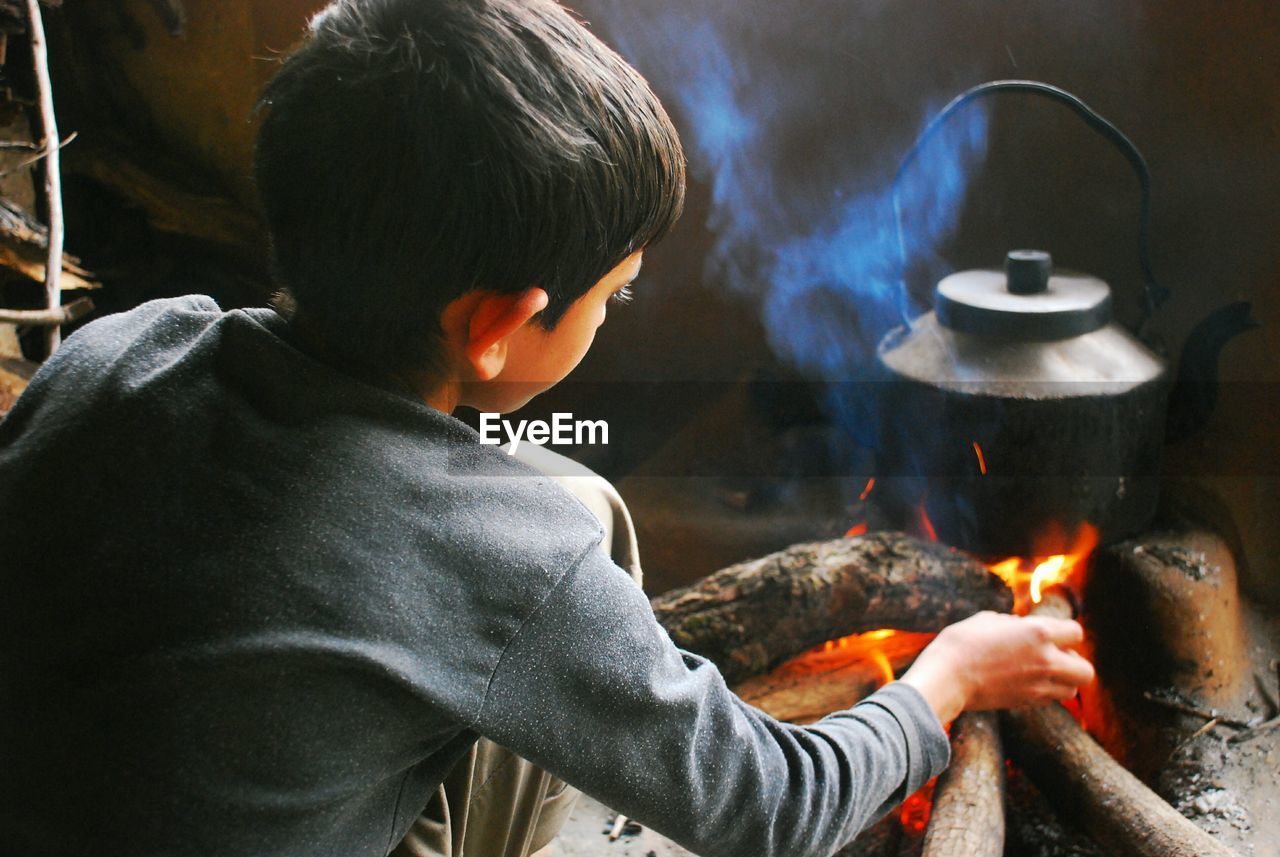 Boy preparing chai in kettle on fire