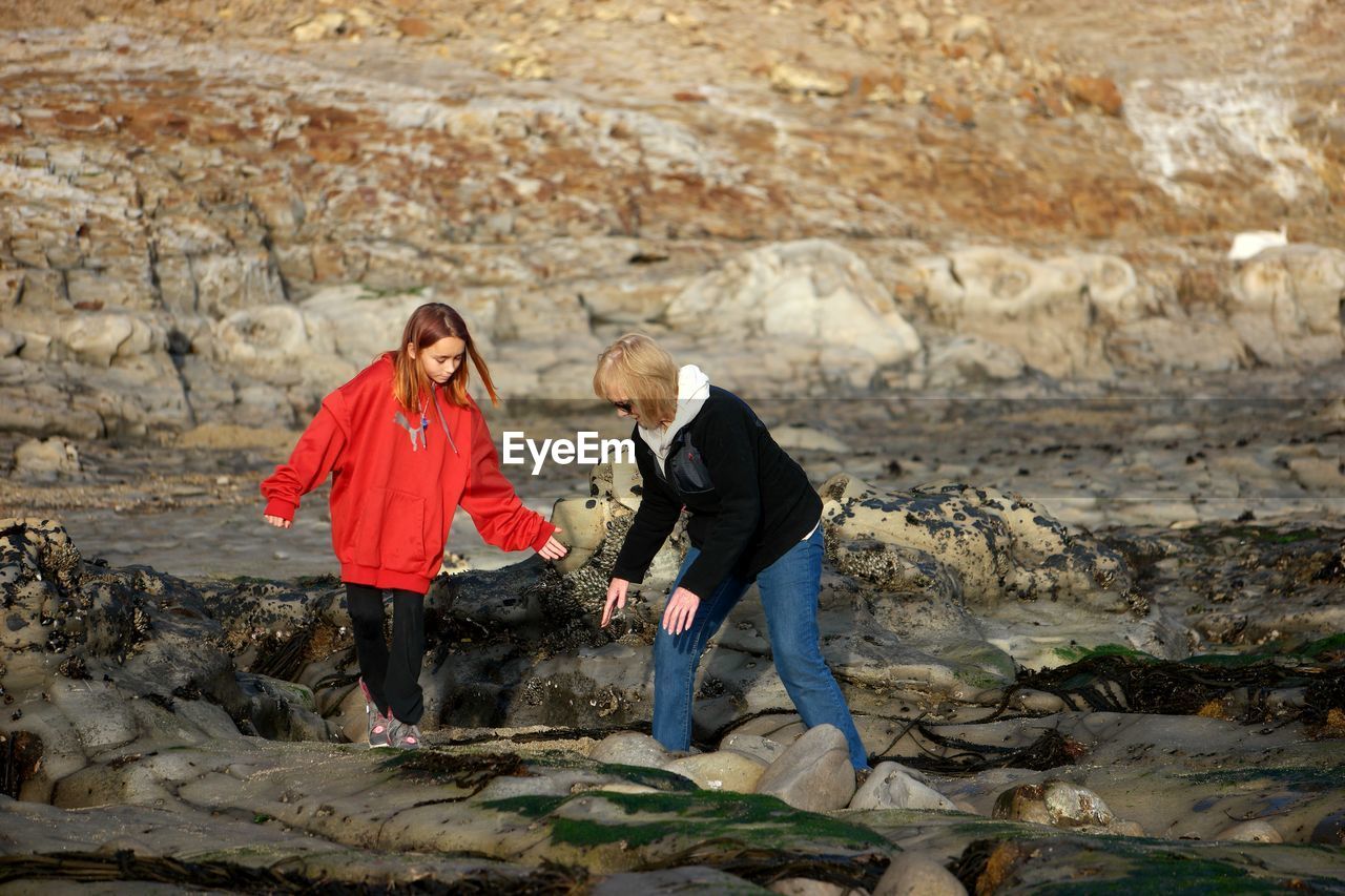Grandmother and granddaughter walking on rocks at beach
