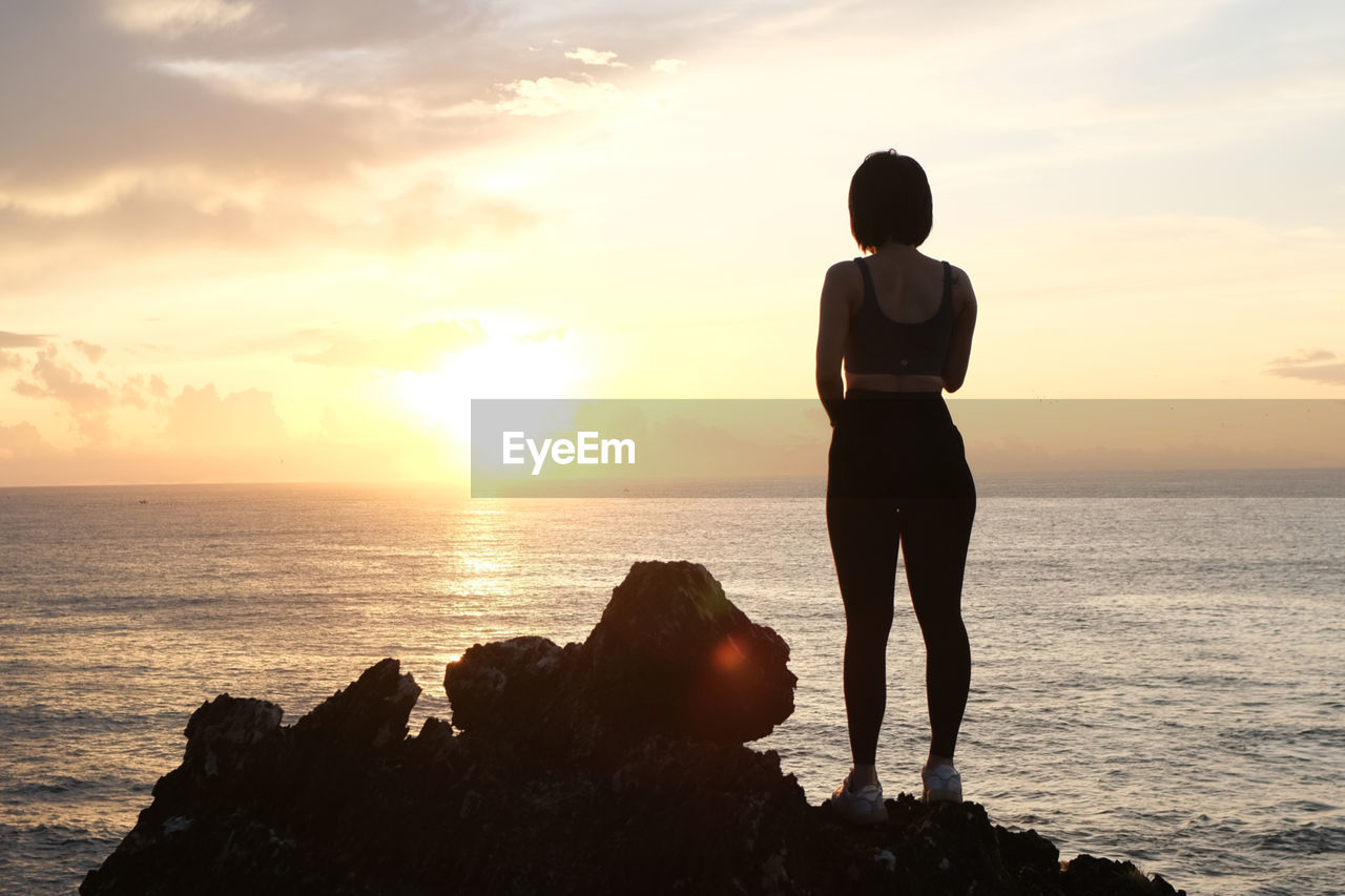 rear view of silhouette woman standing on beach against sky during sunset